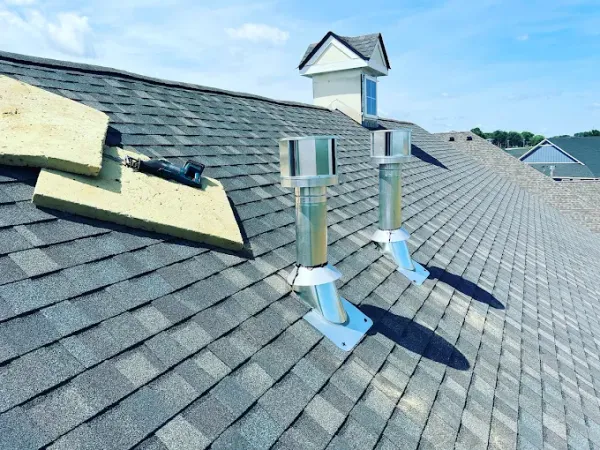 Two stainless vent terminations on an asphalt-shingle roof, photographed from the ridge