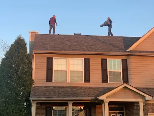 Two technicians on the roof of a two-story house, seen from the street