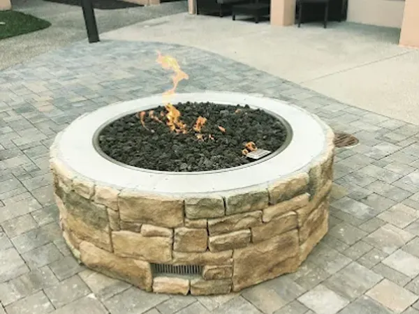 A round stone gas fire pit burning on a paver patio