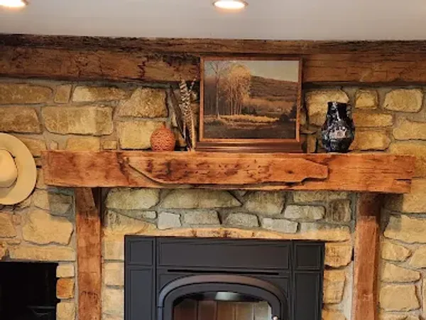 A black fireplace insert in a rustic fieldstone surround with a heavy timber mantel