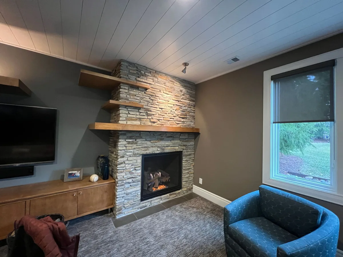 A gas fireplace burning in a stacked-stone wall with a floating wood mantel, a Central Indiana install