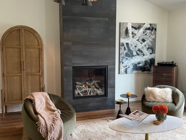 A direct-vent gas fireplace in a floor-to-ceiling dark modern surround with a black chandelier
