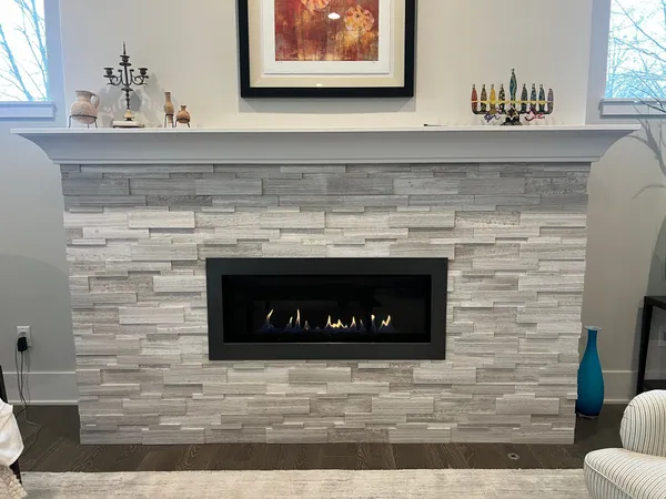 A linear direct-vent gas fireplace in a white stacked-stone surround with a grey mantel