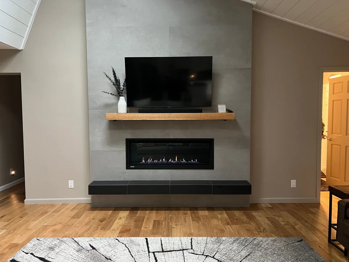 A linear direct-vent gas fireplace in a stone surround with a floating wood mantel