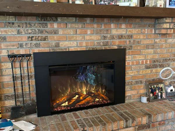 An electric fireplace insert glowing in a brick fireplace under a wood mantel with a wall clock
