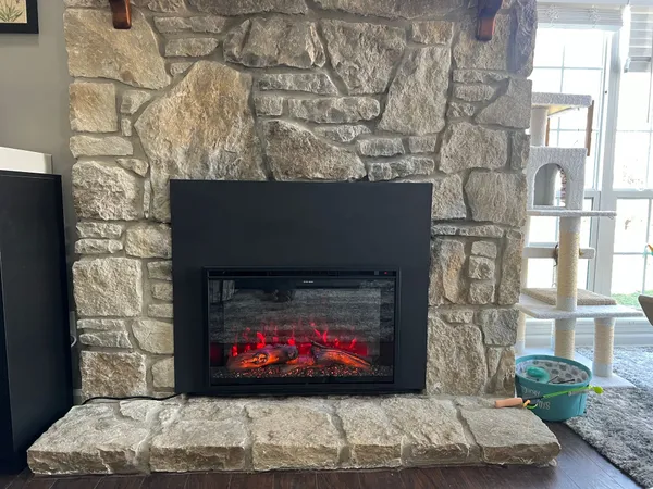 An electric insert glowing in a fieldstone fireplace with a stone hearth