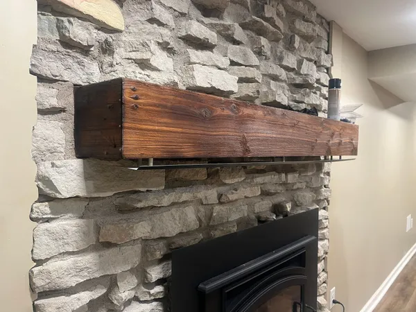 A reclaimed timber mantel with a black mantel shield over a stacked-stone fireplace