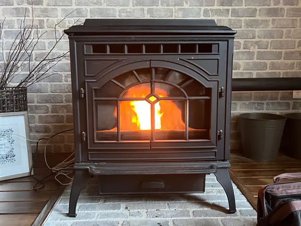 A cast-iron pellet stove burning in a whitewashed brick corner on a tile hearth pad