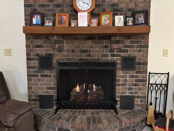 A vent-free gas log set burning in a brick fireplace under a wood mantel lined with family photos