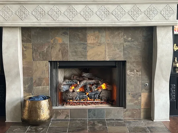 A vented gas log set burning inside a slate-tiled fireplace with a carved cast-stone mantel