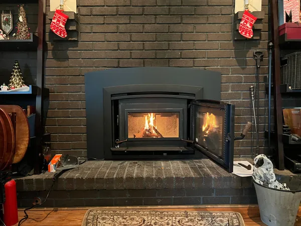 A wood-burning insert glowing in a painted brick fireplace with stockings on the mantel