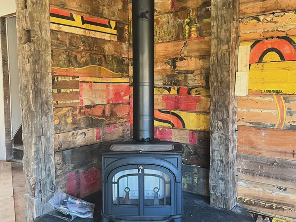 A black wood stove on a stone hearth pad in front of a painted mural wall