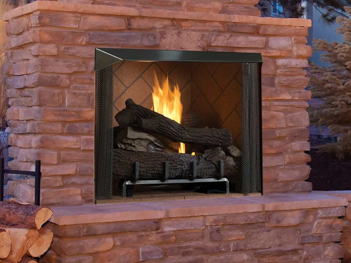 A Superior VRE6036 outdoor fireplace burning in a red stone surround at dusk (manufacturer photo)