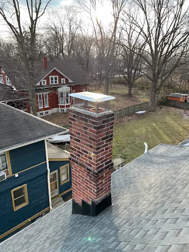 A brick chimney with a new stainless cap and fresh flashing, photographed from the roof in low winter sun, a Kindled Timber job